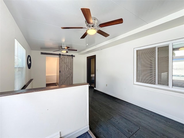 interior space with a barn door, a wealth of natural light, ceiling fan, and dark hardwood / wood-style floors