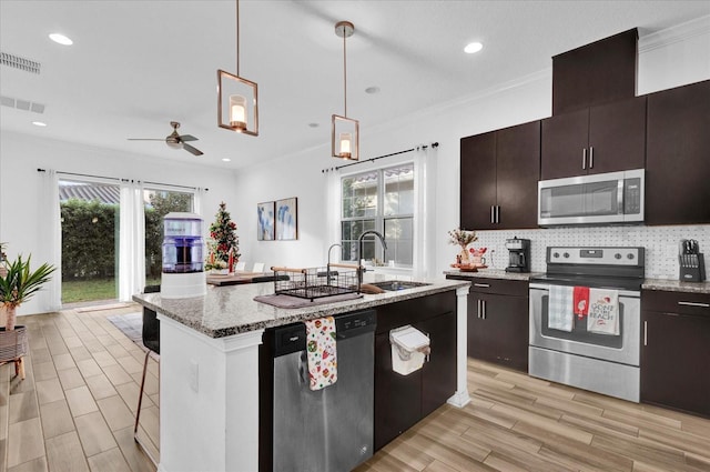 kitchen with ceiling fan, sink, hanging light fixtures, stainless steel appliances, and an island with sink