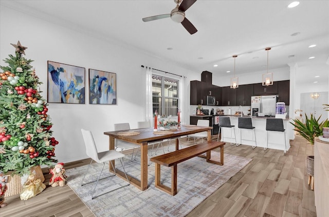 dining area with ceiling fan, crown molding, sink, and light wood-type flooring