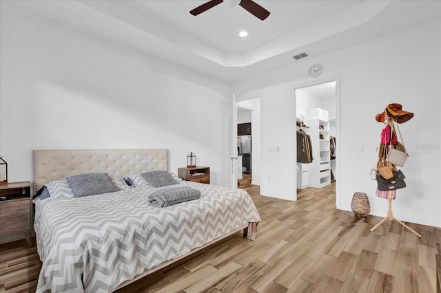 bedroom featuring a spacious closet, ceiling fan, a tray ceiling, a closet, and light wood-type flooring