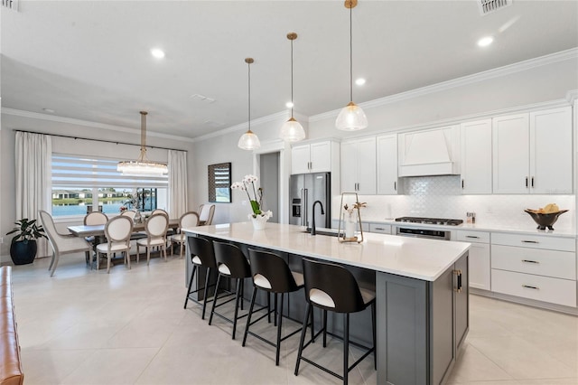 kitchen with stainless steel appliances, decorative light fixtures, a kitchen island with sink, white cabinets, and custom range hood