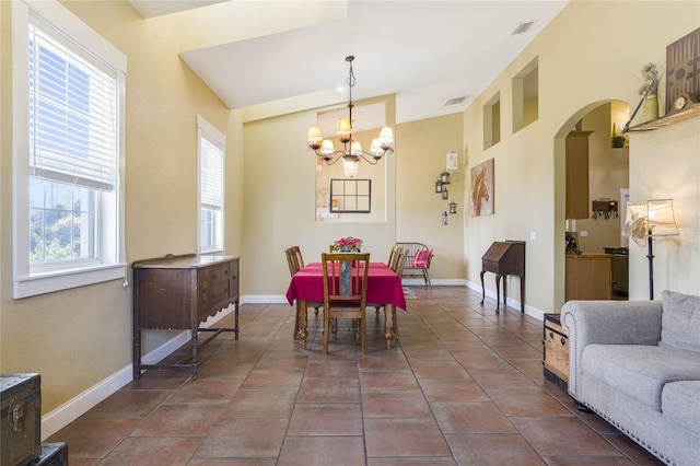 dining area with dark tile patterned floors, vaulted ceiling, and an inviting chandelier