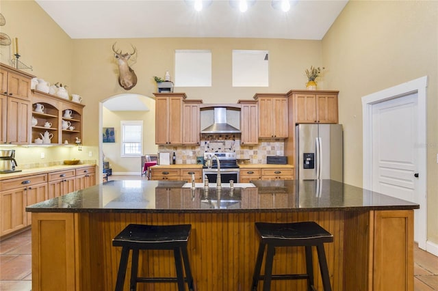 kitchen featuring sink, stainless steel appliances, wall chimney range hood, a kitchen bar, and a kitchen island with sink