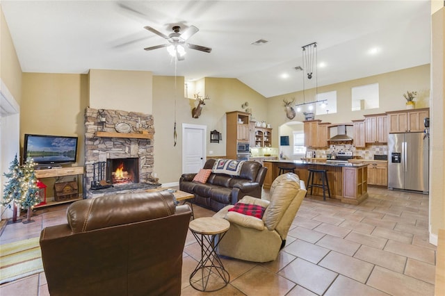 tiled living room featuring ceiling fan, a stone fireplace, and high vaulted ceiling