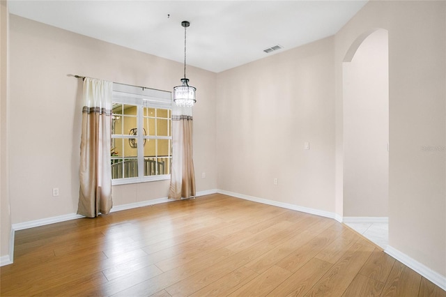 empty room with light wood-type flooring and a chandelier