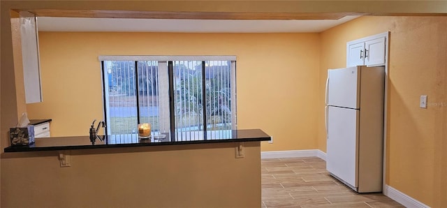 kitchen featuring white cabinetry, a kitchen bar, kitchen peninsula, and white refrigerator