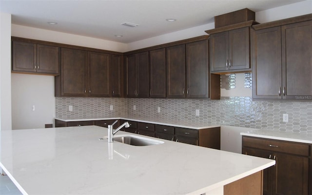 kitchen with dark brown cabinets, sink, an island with sink, and tasteful backsplash