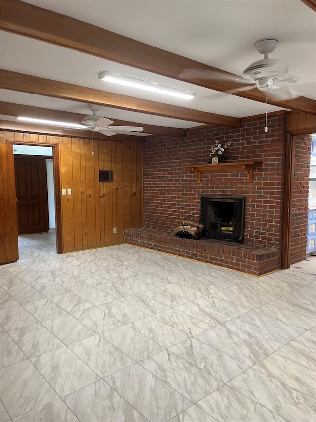 unfurnished living room with a fireplace, wood walls, beam ceiling, and ceiling fan