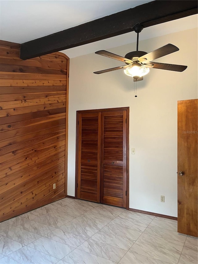 unfurnished bedroom featuring ceiling fan, beamed ceiling, and wood walls