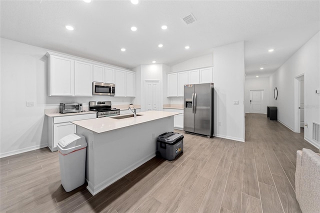 kitchen with appliances with stainless steel finishes, light wood-type flooring, sink, white cabinets, and an island with sink