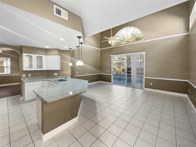 kitchen with light stone counters, ceiling fan, sink, pendant lighting, and white cabinets