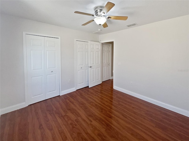 unfurnished bedroom featuring ceiling fan, dark hardwood / wood-style flooring, and two closets