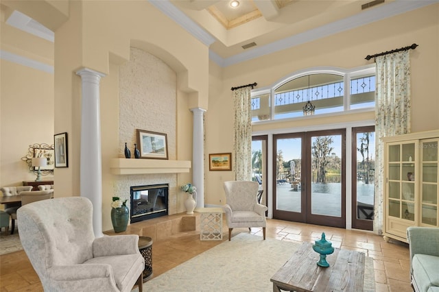 living room featuring crown molding, a tile fireplace, a towering ceiling, french doors, and ornate columns