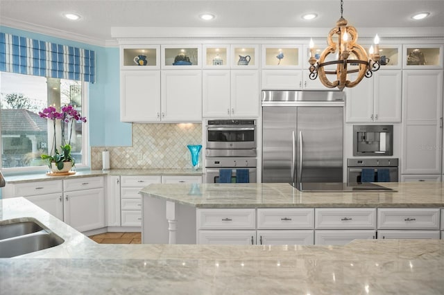 kitchen with light stone counters, tasteful backsplash, built in appliances, pendant lighting, and white cabinets