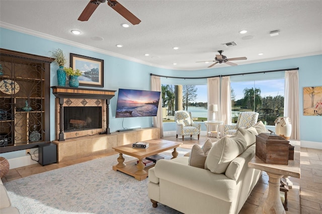 living room featuring a tiled fireplace, crown molding, ceiling fan, and a textured ceiling