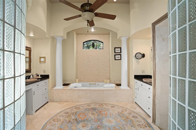 bathroom with tiled tub, ceiling fan, vanity, tile patterned floors, and ornate columns