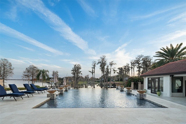 pool at dusk with a water view and a patio area