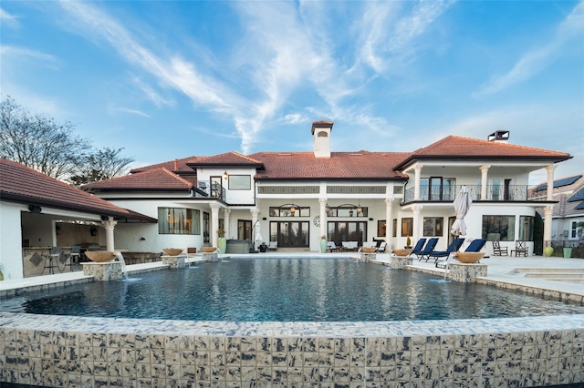 rear view of property with a bar, a patio area, pool water feature, and a balcony