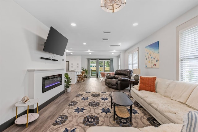 living room with a glass covered fireplace, wood finished floors, visible vents, and recessed lighting