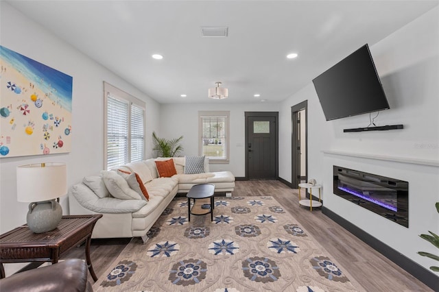 living room featuring light wood-style floors, recessed lighting, visible vents, and a glass covered fireplace