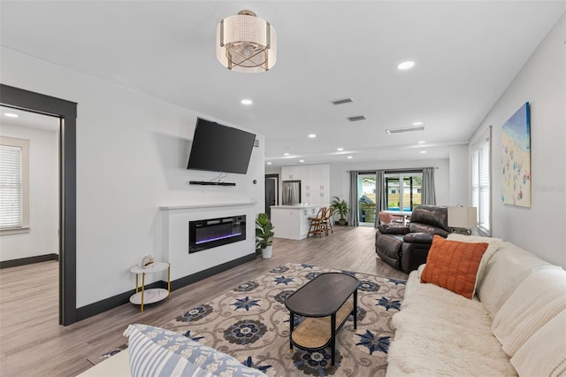 living room featuring baseboards, light wood finished floors, a glass covered fireplace, and recessed lighting