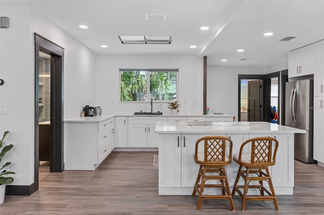 kitchen featuring a sink, white cabinets, a kitchen breakfast bar, freestanding refrigerator, and a center island