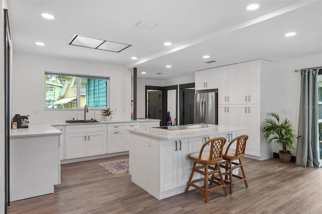 kitchen featuring light countertops, freestanding refrigerator, white cabinetry, a sink, and a kitchen bar