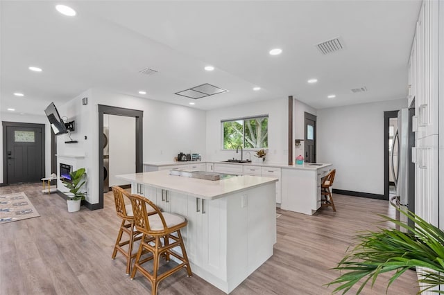 kitchen with a breakfast bar, a sink, white cabinetry, light countertops, and a center island