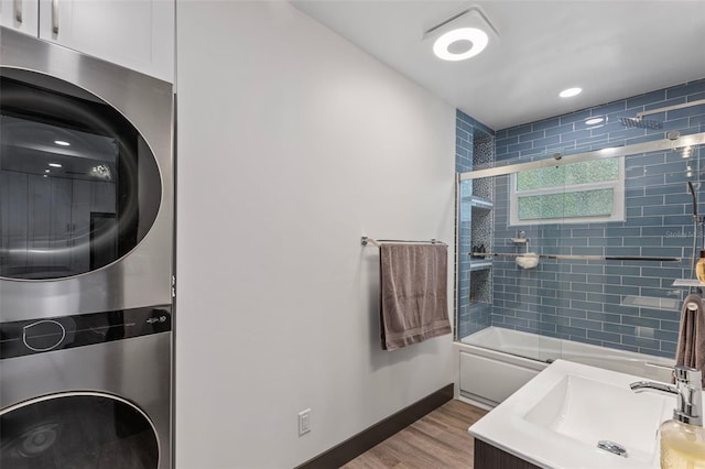 bathroom featuring bath / shower combo with glass door, stacked washer and dryer, vanity, wood finished floors, and baseboards