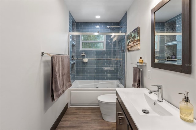 bathroom featuring enclosed tub / shower combo, toilet, wood finished floors, vanity, and baseboards