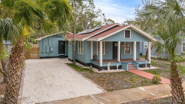 bungalow-style house with covered porch, solar panels, gravel driveway, and fence