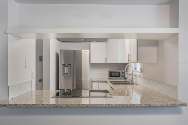 kitchen with light stone countertops, appliances with stainless steel finishes, white cabinetry, sink, and kitchen peninsula