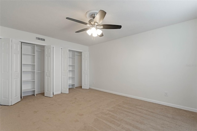 unfurnished bedroom featuring multiple closets, ceiling fan, and light colored carpet