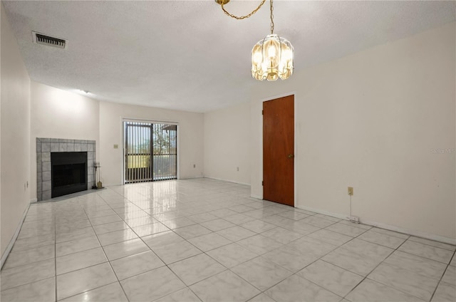 unfurnished living room with a fireplace, light tile patterned floors, a textured ceiling, and an inviting chandelier