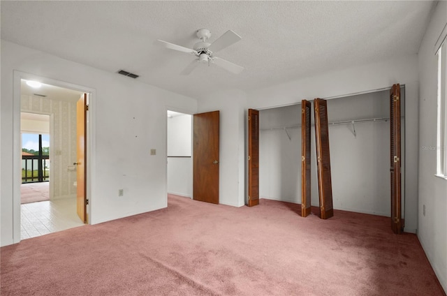 unfurnished bedroom featuring light carpet, a textured ceiling, two closets, and ceiling fan