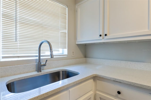 kitchen with light stone countertops, white cabinetry, and sink