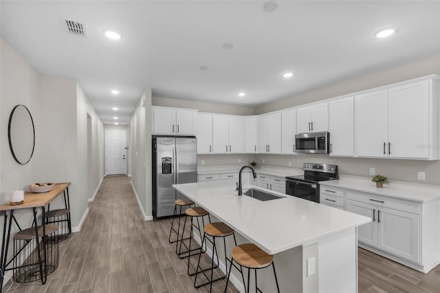 kitchen featuring a kitchen bar, appliances with stainless steel finishes, sink, a center island with sink, and white cabinetry