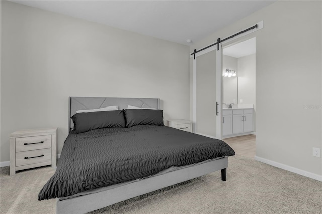 bedroom with a barn door, light carpet, sink, and ensuite bath