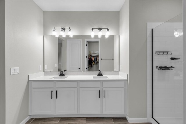 bathroom featuring double vanity, a stall shower, baseboards, and a sink