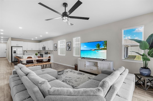 living area with light wood-style floors, baseboards, a ceiling fan, and recessed lighting