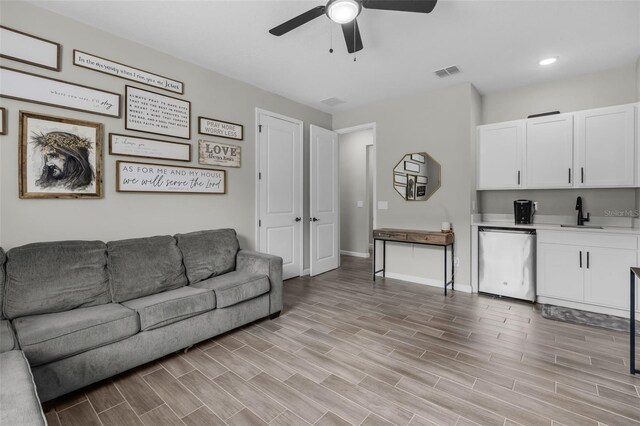 living room with baseboards, wood finish floors, visible vents, and a ceiling fan