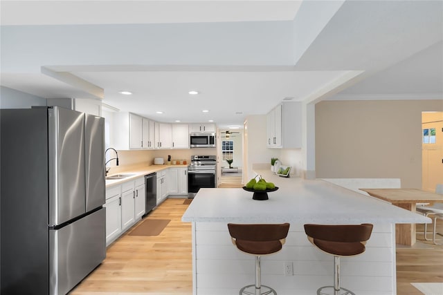 kitchen with a peninsula, a breakfast bar, white cabinets, light countertops, and appliances with stainless steel finishes