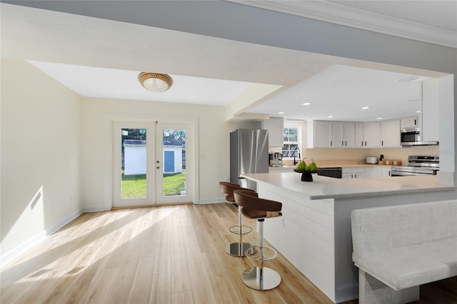 kitchen featuring white cabinets, a kitchen breakfast bar, stainless steel appliances, light countertops, and a wealth of natural light