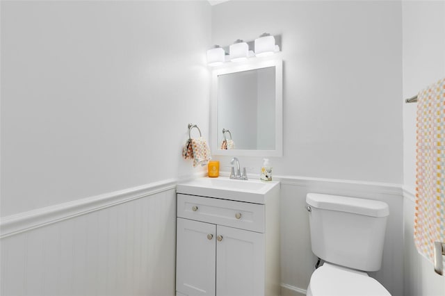 half bathroom with a wainscoted wall, vanity, and toilet