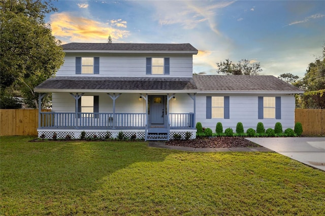 view of front facade with a porch, a front yard, fence, and a shingled roof