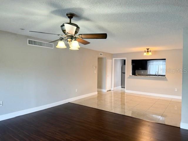 unfurnished living room featuring ceiling fan, sink, a textured ceiling, and light hardwood / wood-style flooring