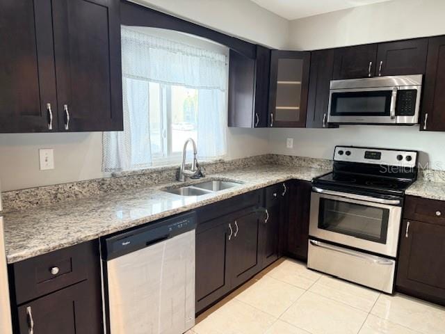 kitchen featuring light stone countertops, appliances with stainless steel finishes, dark brown cabinetry, sink, and light tile patterned floors