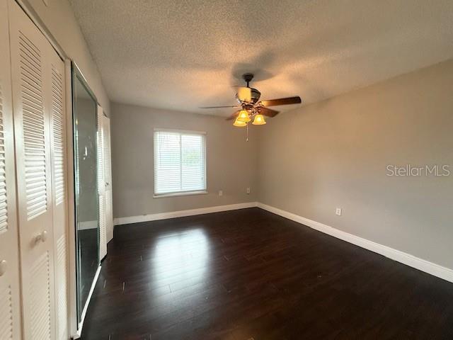 unfurnished bedroom with a textured ceiling, dark hardwood / wood-style flooring, a closet, and ceiling fan