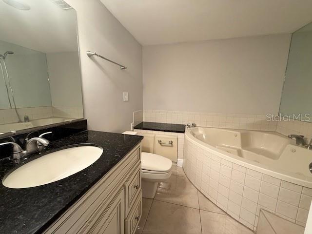 bathroom with tile patterned flooring, vanity, a relaxing tiled tub, and toilet