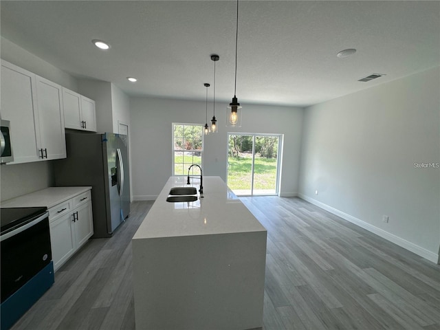 kitchen featuring pendant lighting, white cabinets, wood-type flooring, and an island with sink